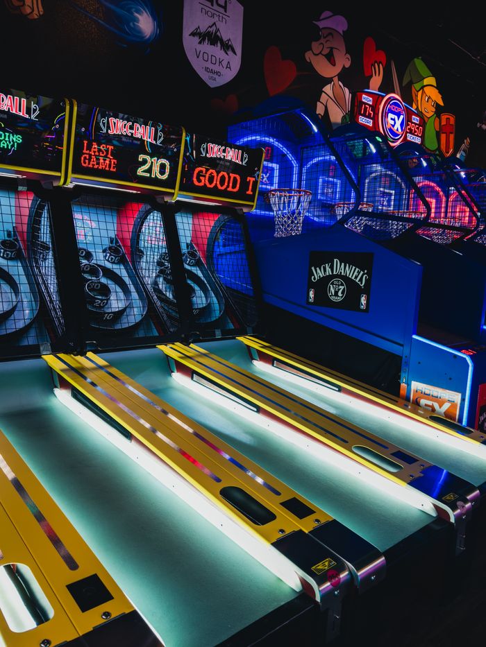 Colorful arcade with skeeball and basketball games under neon lights.