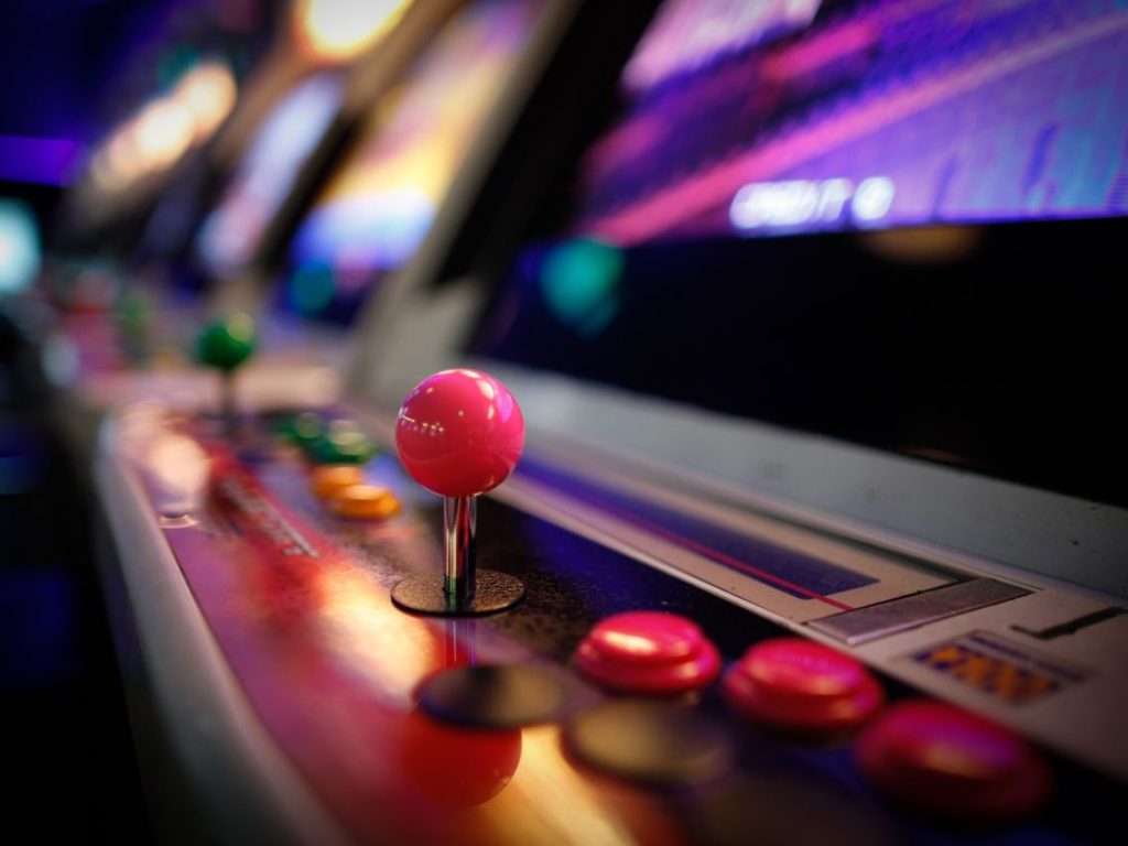 Our Games Close-up of a colorful vintage arcade machine with glowing joysticks and buttons in a dimly lit game room.